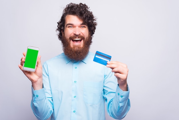 Exciting young man holding credit card  and a phone looking at the camera