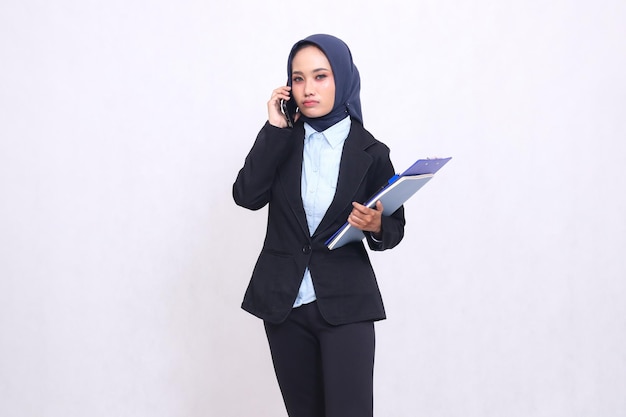 Exclusieve Aziatische kantoorvrouw met een hijab staat somber naar iemands telefooncamera en draagt een