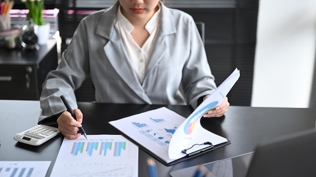 Исполнительная деловая женщина, использующая калькулятор и анализирующая финансовый график на своем рабочем месте