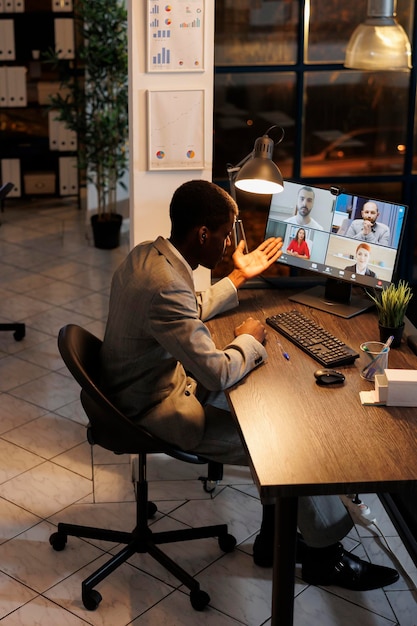 Executive manager having remote conversation with team during online videocall meeting conference, discussing marketing strategy. Diverse coworkers working late at night in startup office