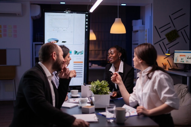 Executive manager woman explaining management statistics working at company strategy overtime in office meeting room. Diverse multi-ethnic businesspeople teamwork brainstorming ideas in evening