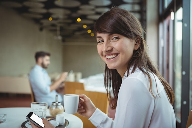 Executive met behulp van mobiele telefoon terwijl het drinken van koffie in cafetaria