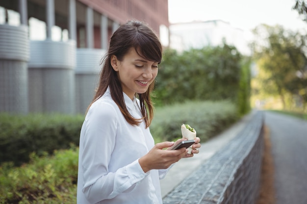 Executive met vegetarische roll tijdens het gebruik van mobiele telefoon op de weg