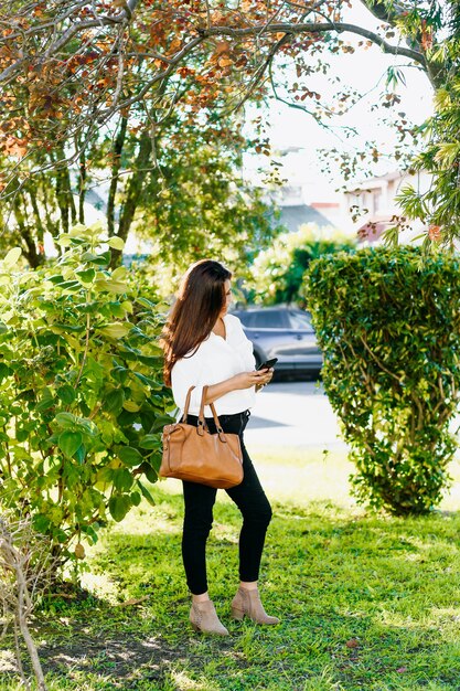 Executive woman walking with her cell phone and purse in the park