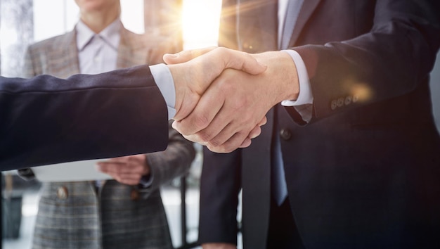 Executives shaking hands in front of their manager and a colleague