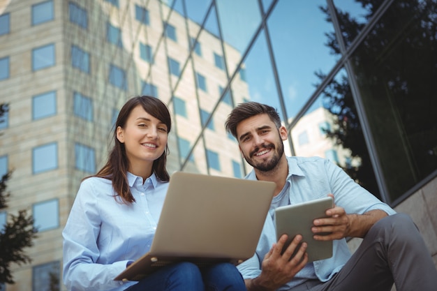 Executives using laptop and digital tablet outside office building