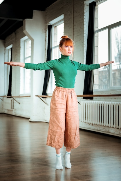 Exercise for balance. Pretty red haired girl wearing orange trousers looking focused while doing balancing exercise