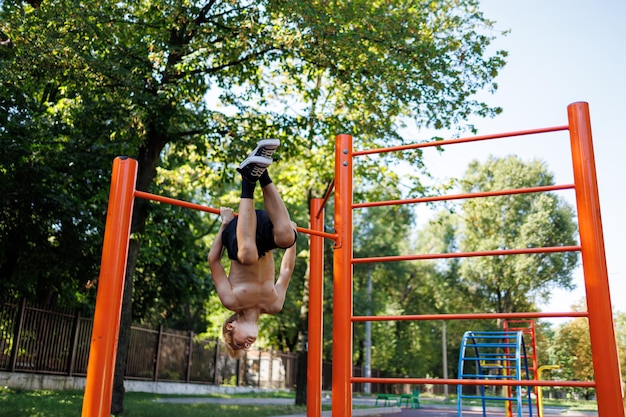 Exercise boy hangs his head down Street workout on a horizontal bar in the school park