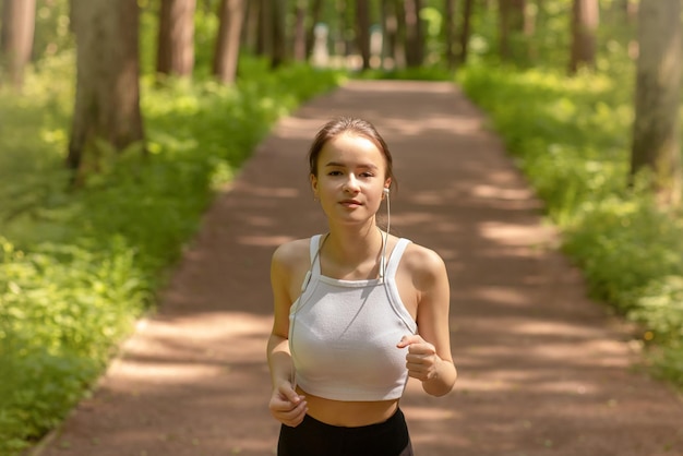 Esercizio all'aria aperta la ragazza corre in cuffia nel parco tra gli alberi