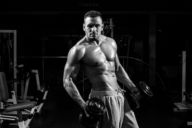 Exercise in gym. Sports workout. Fitness man in focused on lifting a dumbbell.