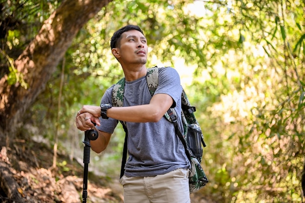 Exhausted Asian man with backpack and trekking gear walking through the forest exploring trekking