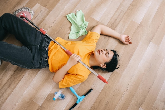 Photo exhausted asian woman laying on the floor feeling tired after cleaning the house