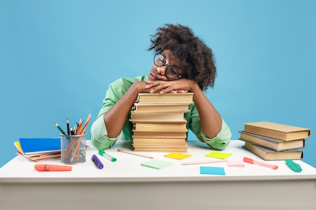 Photo exhausted black male student sleeping on desk on stacks of books being tired while preparing for