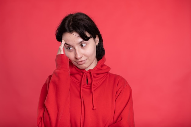 Exhausted brunette girl in red hoodie touches forehead looking at front