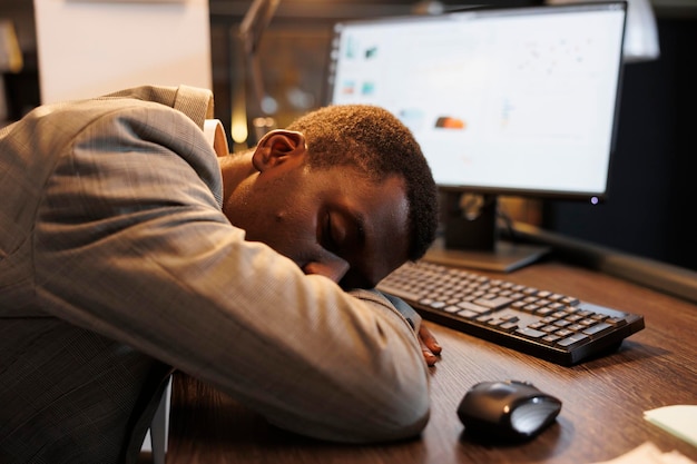 Exhausted entrepreneur with burnout syndrome resting at work after finishing company strategy. Tired fatigued executive manager sleeping on desk in office workspace after overtime work