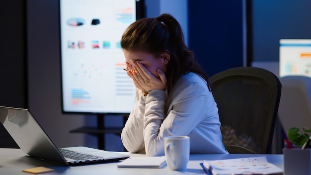 Exhausted freelancer sleeping in front of laptop working in modern start up company office late at night. Stressed employee using modern technology network wireless doing overtime closing eyes.