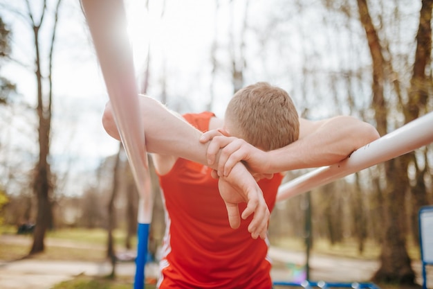 Exhausted guy in red tshirt collapsing after a rigorous parallel bars workout