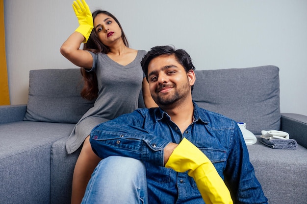 Exhausted indian woman and tired man in gloves sitting on sofa,feeling very tiredness after cleaning at home.