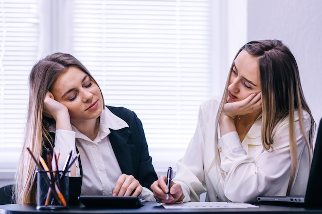 Exhausted male and female students sitting at desk and feeling h