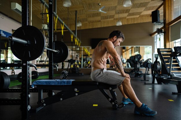 Photo exhausted man sitting on a bench of a gym