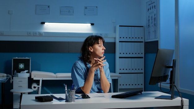 Exhausted nurse in blue uniform working over hours in hospital\
office analyzing patient illness report typing medical expertise on\
computer during checkup visit. tires stressed checking health care\
do