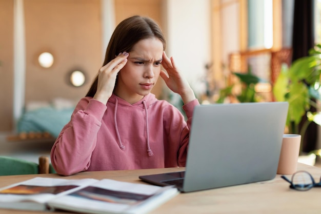 Exhausted schoolgirl suffering from headache overworking having too much online homework looking at laptop