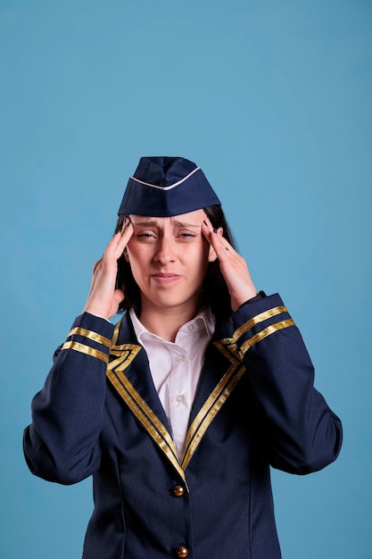 Exhausted stewardess having migraine symptom, touching temples with fingers, looking at camera with grimace. Sick flight attendant in aviation uniform suffering from headache