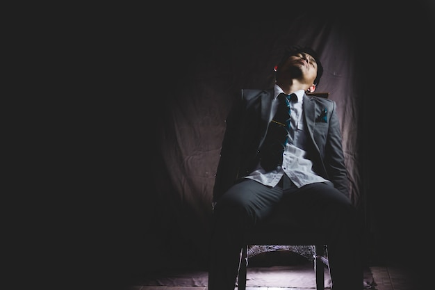 exhausted and tired of asian businessman from overwork, siting and sleep on chair in the dark . 