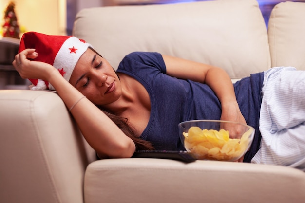 Exhausted woman falling asleep on couch while watching xmas movie