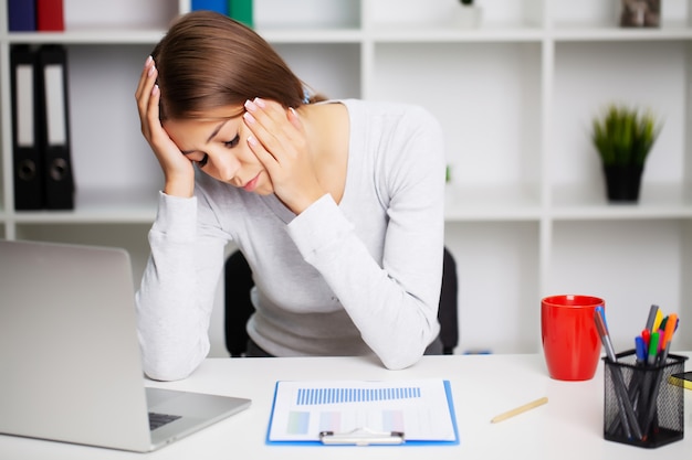 Измученная женщина в офисе страдает от сильной головной боли