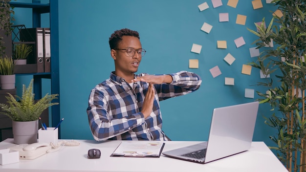 Lavoratore esausto che fa il segno di timeout con le mani davanti allo schermo del laptop, mostrando il simbolo a forma di t per prendersi una pausa dal lavoro d'affari. persona stanca che spera in una pausa dopo essere stata oberata di lavoro.