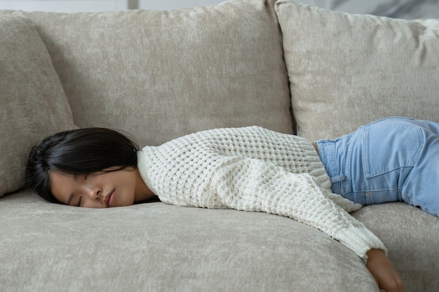 Exhausted young asian woman falls on the sofa a tired lazy woman is sleeping on the couch at home