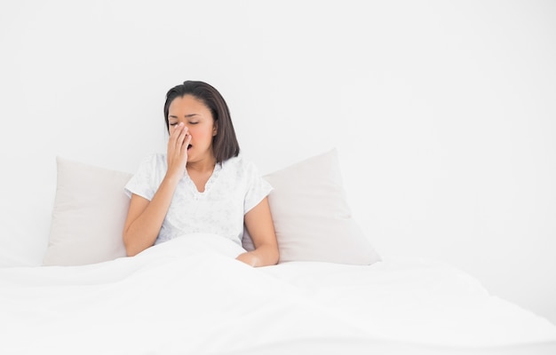 Exhausted young dark haired model yawning lying in her bed