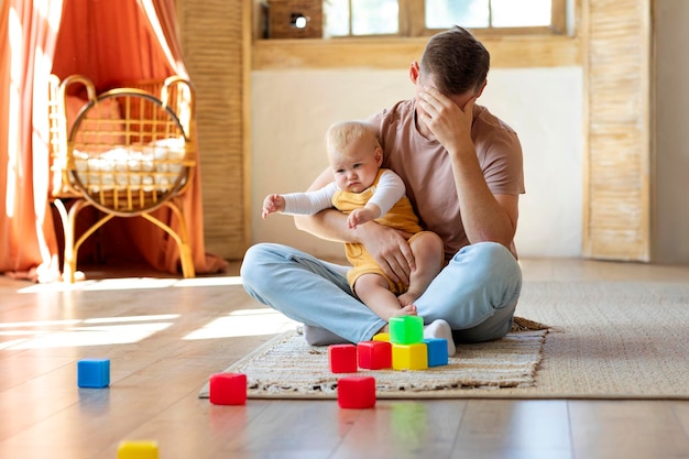 Photo exhausted young father taking care about toddler baby at home