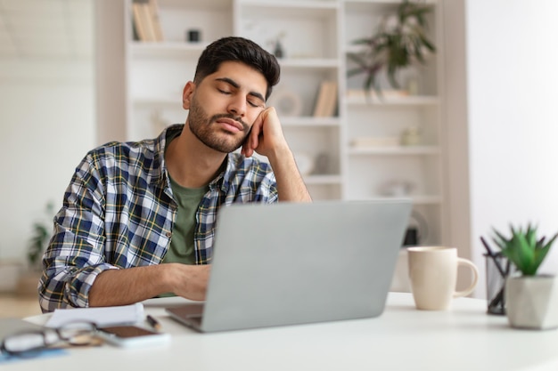 Exhausted young man sleeping at work sitting at desk