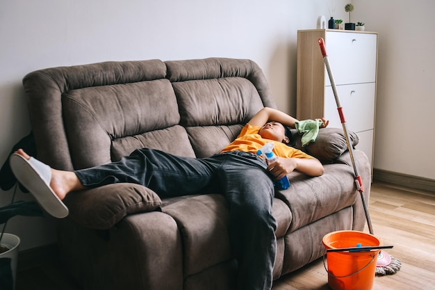 Exhausted young woman falling asleep on sofa feeling tired after cleaning the house