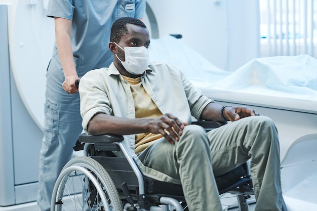 Вытяжной черный пациент с коронавирусом в лицевой маске сидит на инвалидной коляске, которую толкает медсестра после МРТ