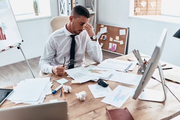 Exhaustion. Top view of tired young man in formalwear working with papers while sitting in the office