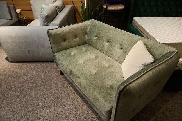 Exhibition of sofas and settees with different quality and\
texture of fabrics in the exhibition hall of a furniture store\
focus on a green small comfortable velour sofa displayed for\
sale