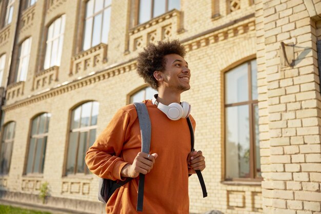 Photo exited teenage boy student walking among buildings of university campus back to offline education process