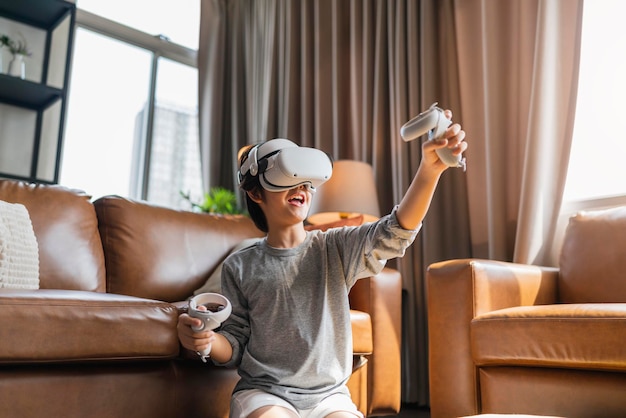 Exiting asian child male boy enjoy metaverse gaming with wearable vr headset with control handle playing sport gaming online in living room at homehome technology young teen using vr technology