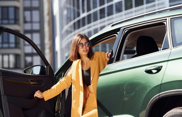 Exits vehicle Young fashionable woman in burgundy colored coat at daytime with her car