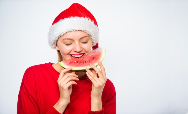 Exotic christmas concept Christmas girl eat watermelon Exotic winter holiday Girl wear santa hat eat slice watermelon white background Celebrate new year summer Summer treats on christmas party