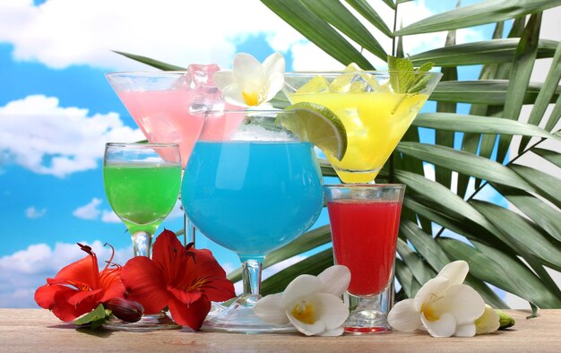 Exotic cocktails and flowers on table on blue sky background