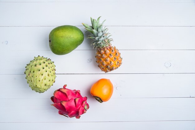 Exotic fresh summer fruits on white. Dragon fruit, pineapple, persimmon, mango, annona cherimola flat lay with free copy space.