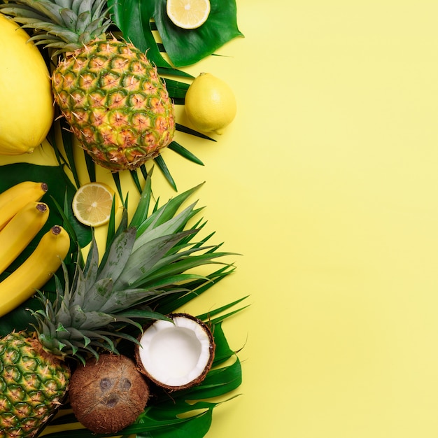 Exotic pineapples, coconuts, banana, melon, lemon, palm and monstera leaves on yellow, violet background 