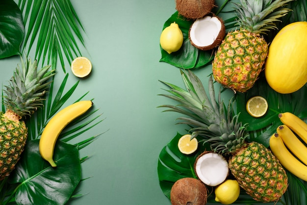 Exotic pineapples, coconuts, banana, melon, lemon, tropical palm and monstera leaves on green. 