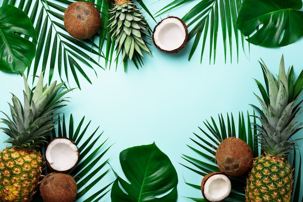 Exotic pineapples, ripe coconuts, tropical palm and green monstera leaves. 