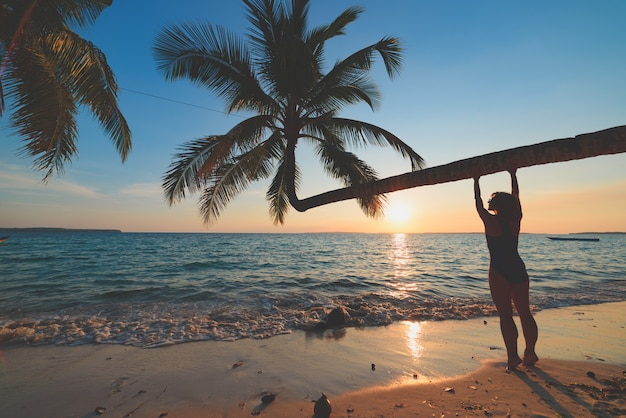 Exotic tropical beach. Woman relaxing under coconut palm frond on scenic white sand beach. Indonesia, Kei islands, Moluccas Maluku, Wab beach