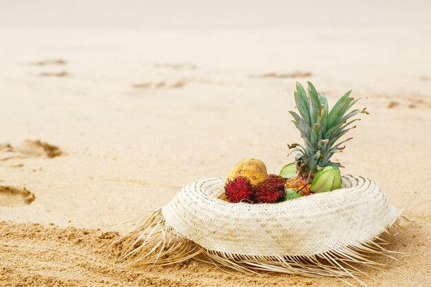 Exotisch fruit in een strohoed bij de oceaan